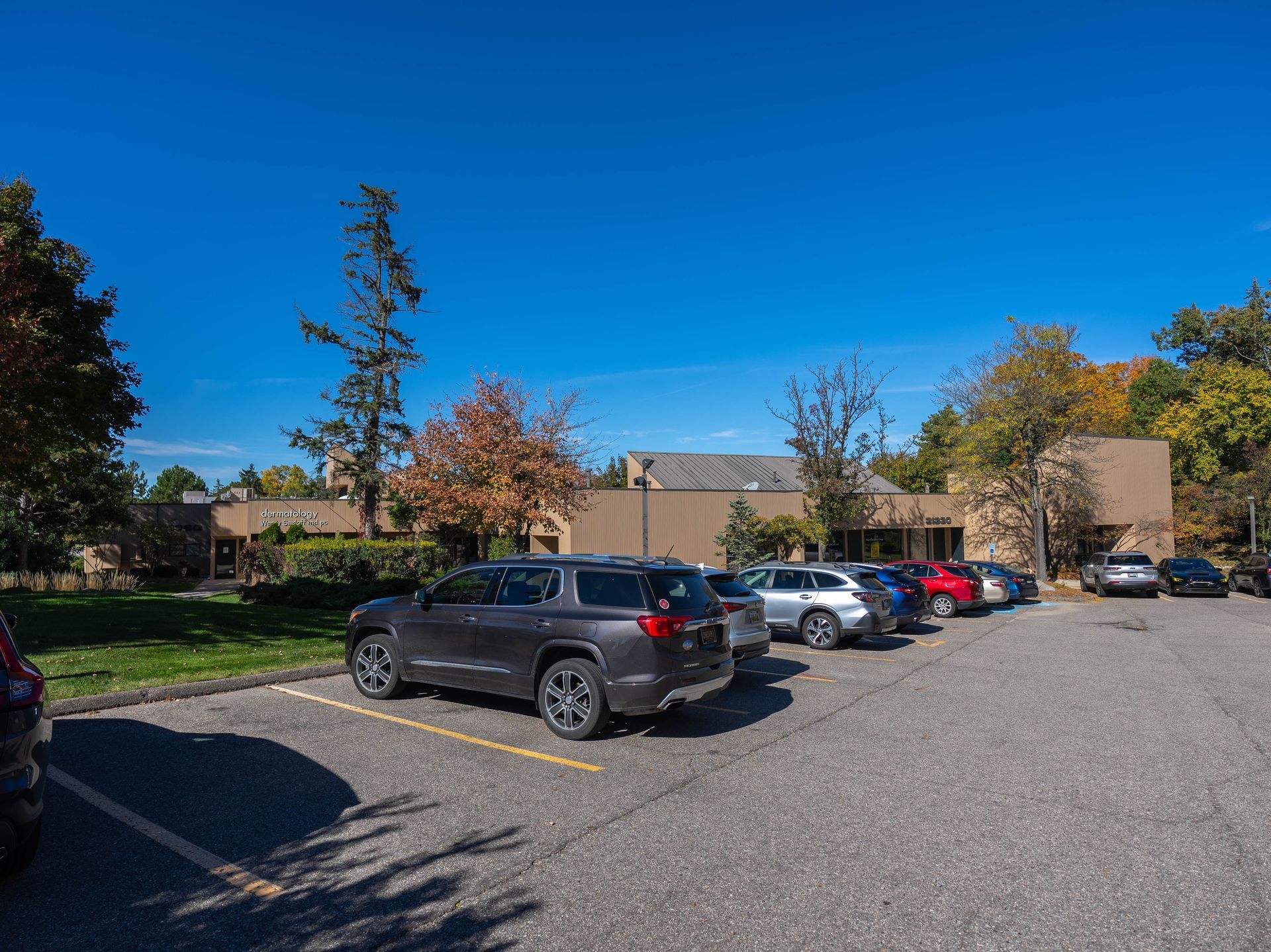 Cars parked in a paved lot in front of a low, beige building under a bright blue sky.