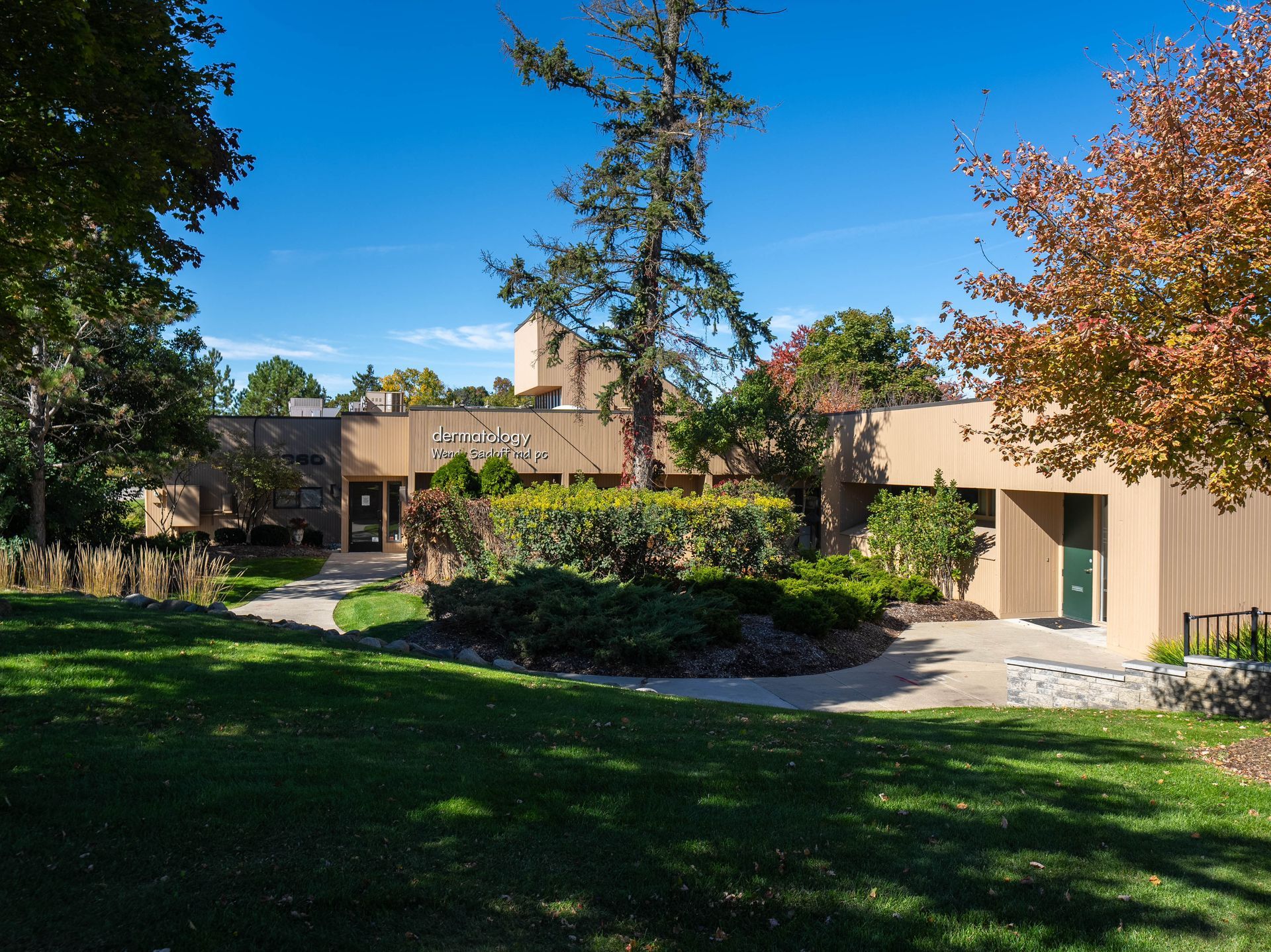 A low, tan building with a green lawn and trees under a blue sky.