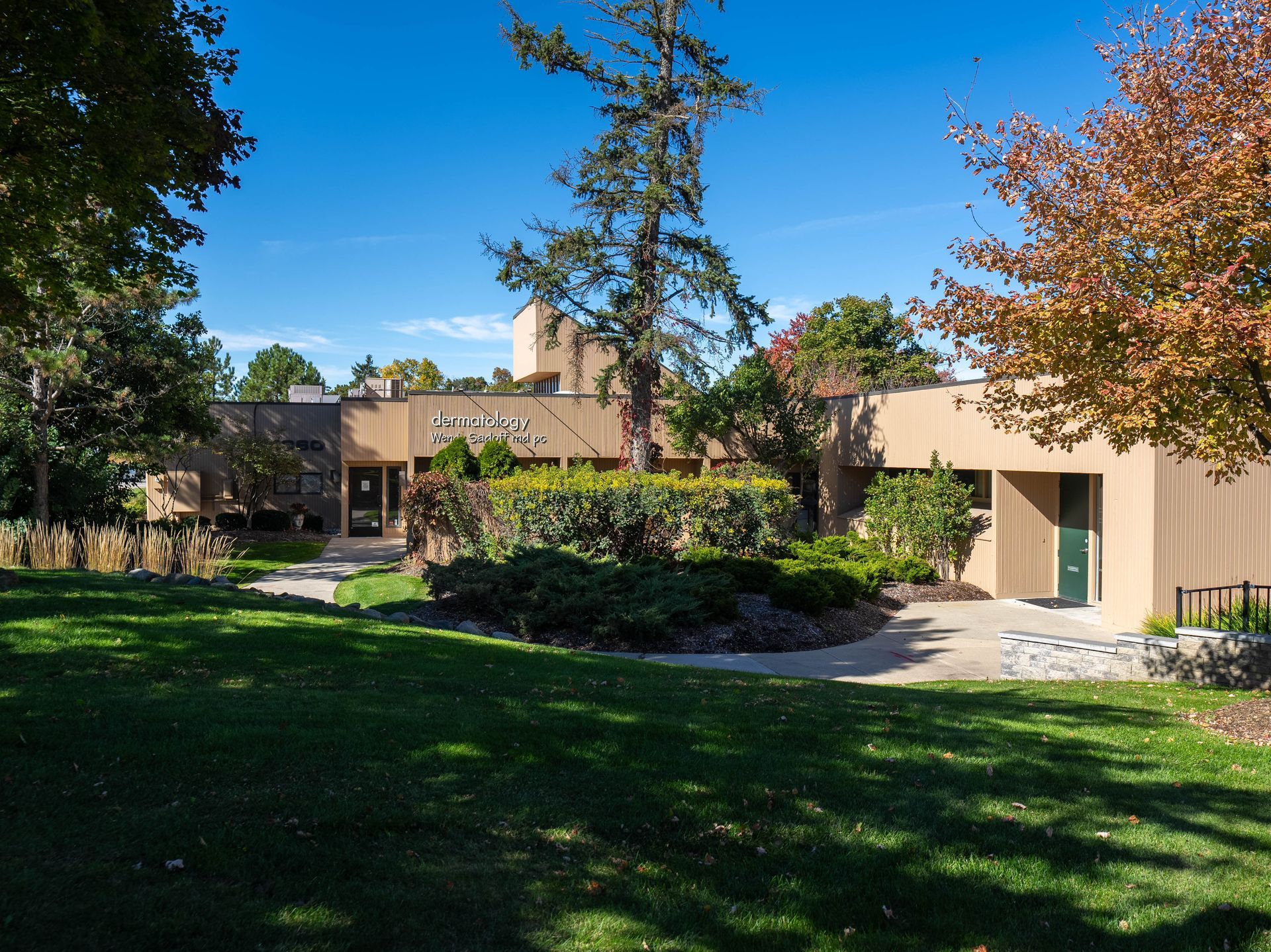 Building exterior with tan walls, green lawn, trees, and blue sky.