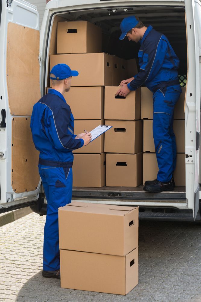 Two Movers in Blue Uniforms Loading Cardboard Boxes Into a White Van — J & V Express Couriers In North Mackay, QLD