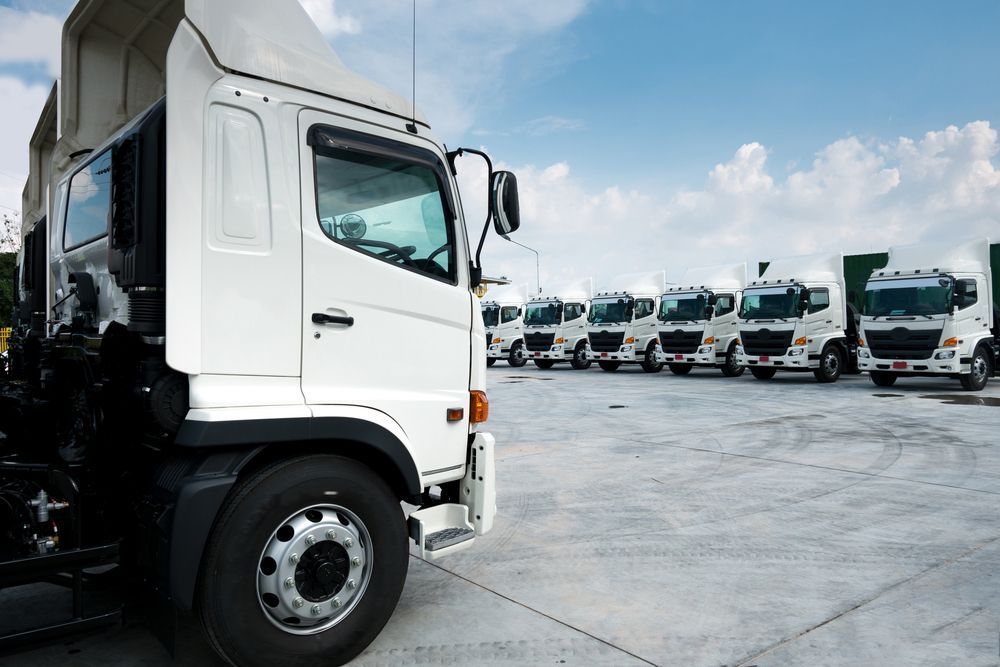 White Delivery Trucks Parked in a Row on a Concrete Lot Under a Blue Sky — J & V Express Couriers In Marian, QLD