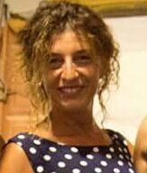 Una donna con un vestito a pois sorride alla telecamera.