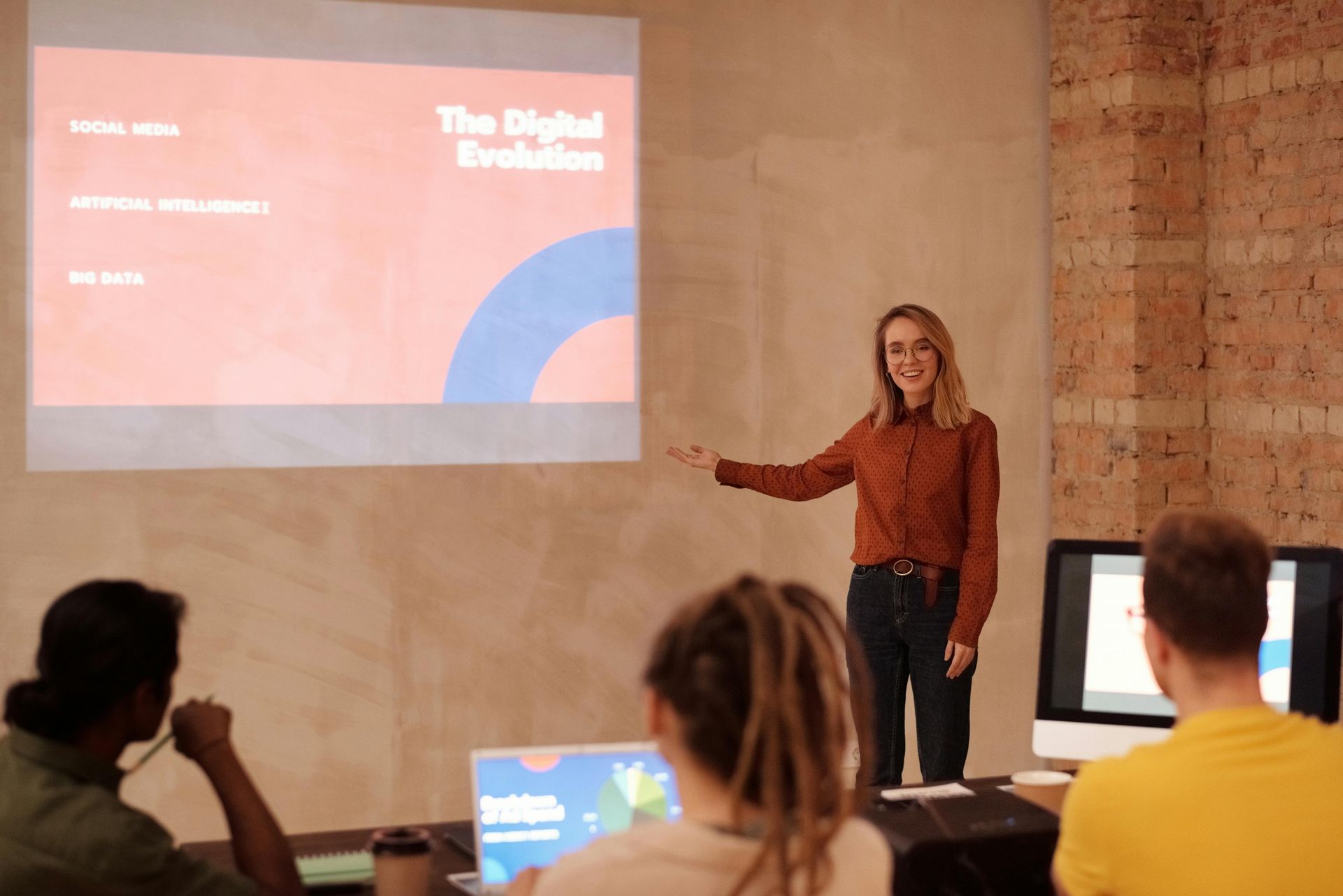 A presenter stands before a projection screen titled