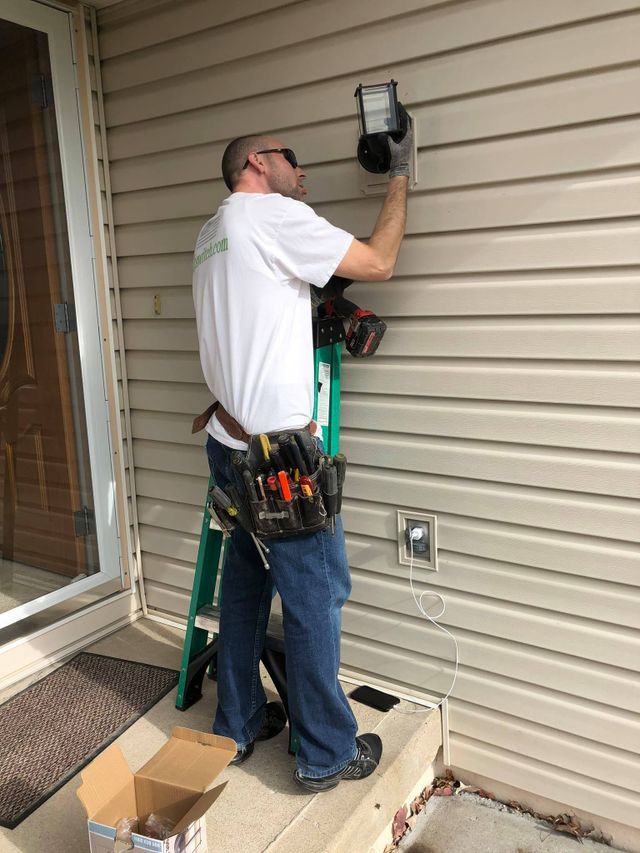 A man is standing on a ladder fixing a light on the side of a house.