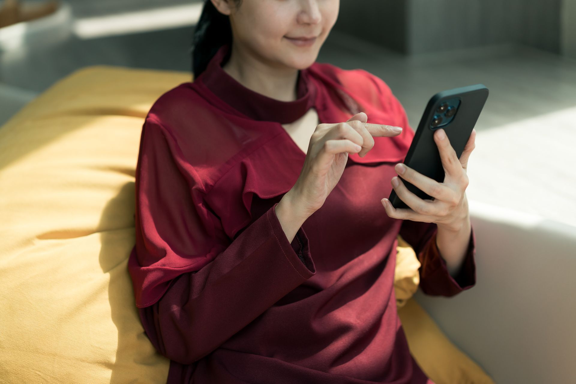 A woman is sitting on a couch using a cell phone.