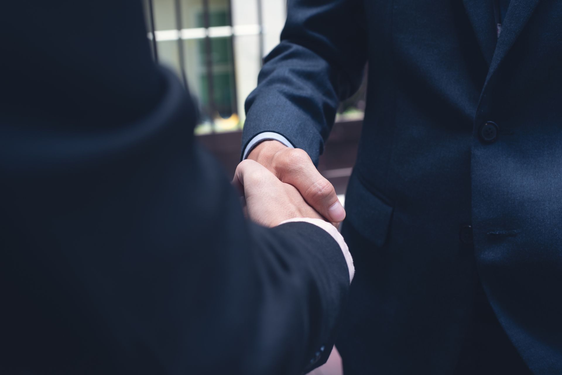 Two men in suits are shaking hands in front of a building.
