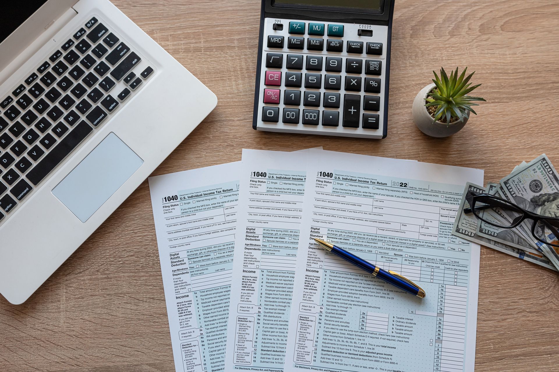 A desk with a laptop , calculator , pen , money and papers