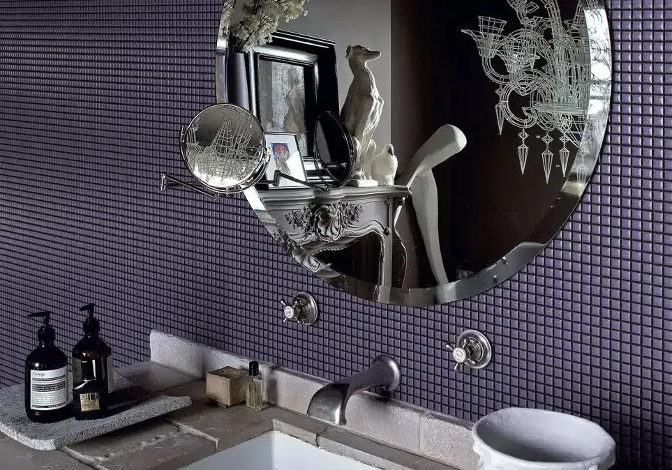 Un bagno con piastrelle viola e uno specchio rotondo