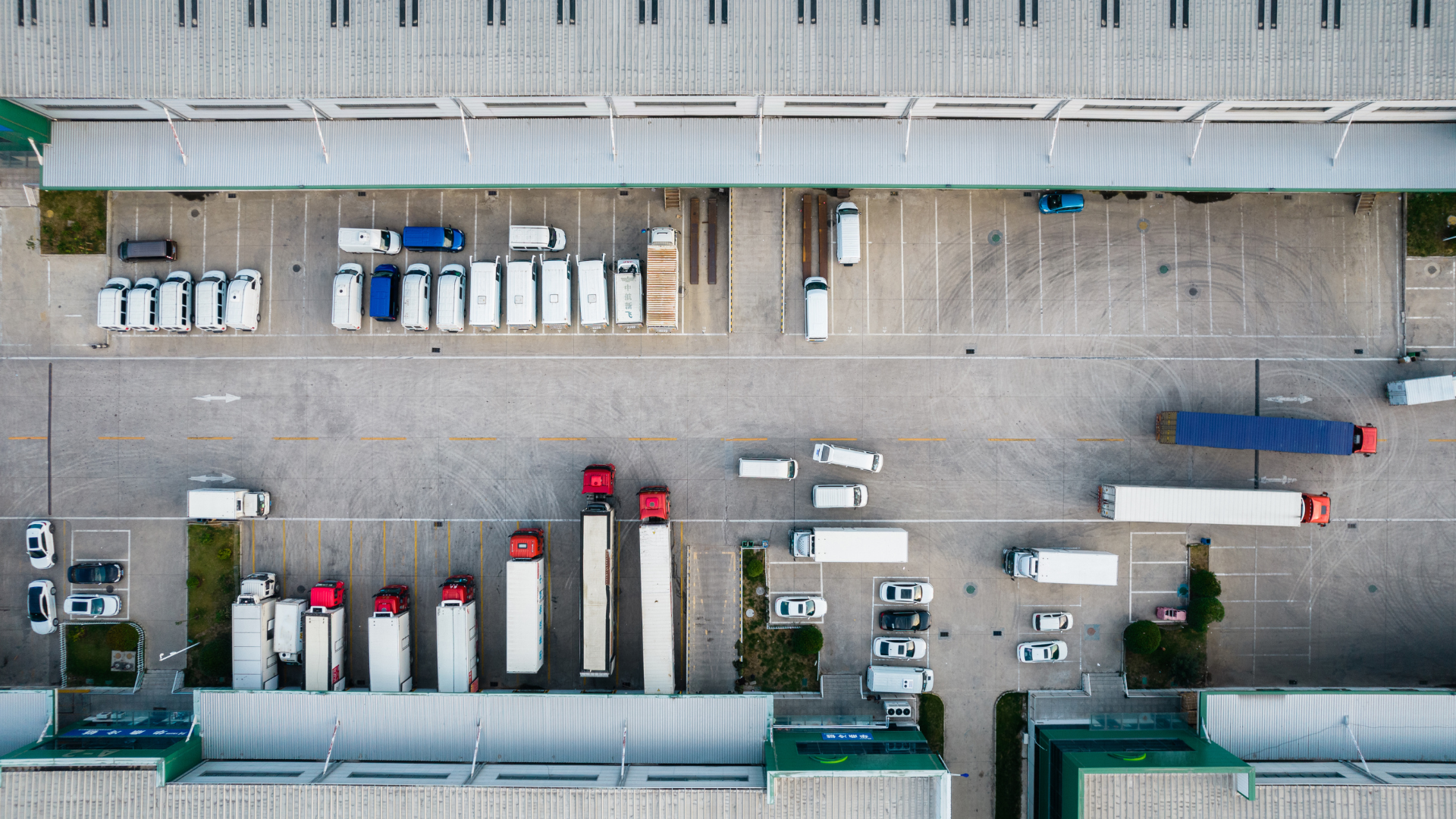 Overhead view of a warehouse loading dock with numerous semi-trucks, vans, and loading bays.