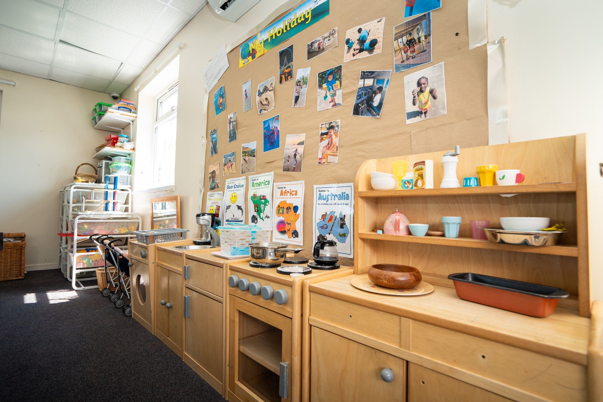 A classroom with a wooden play kitchen and a wall with pictures on it. Gingerbread