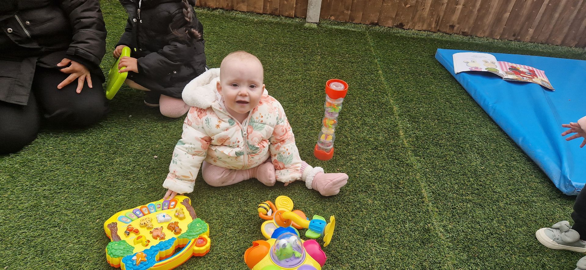 A baby is sitting on the grass surrounded by toys. Gingerbread