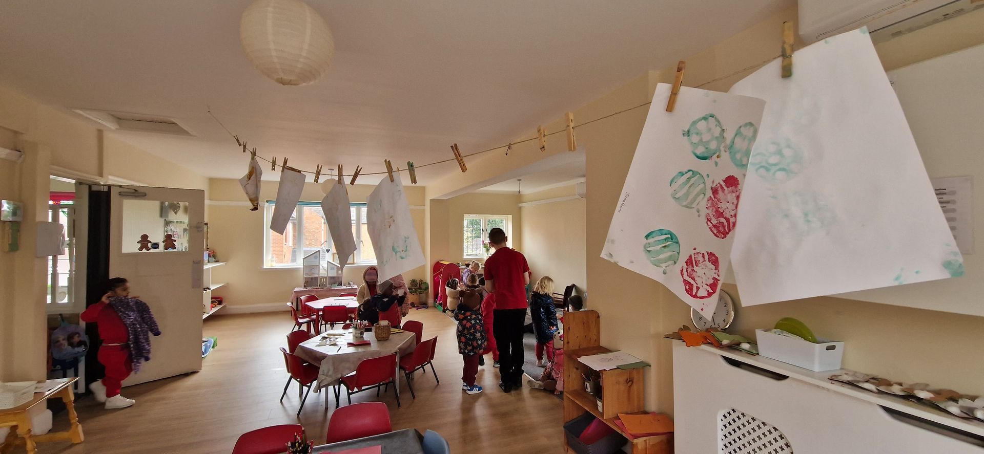 A man in a red shirt is standing in a room with tables and chairs. Gingerbread