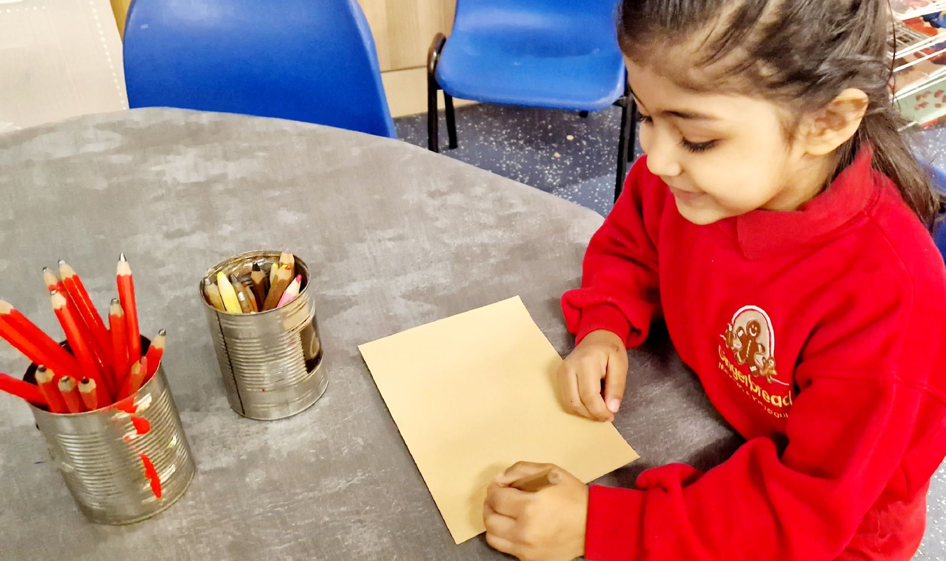 A little girl in a red sweater is sitting at a table writing on a piece of paper. Gingerbread