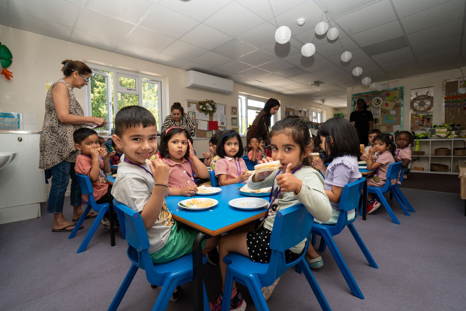 A group of children are sitting at tables in a classroom eating food. Gingerbread