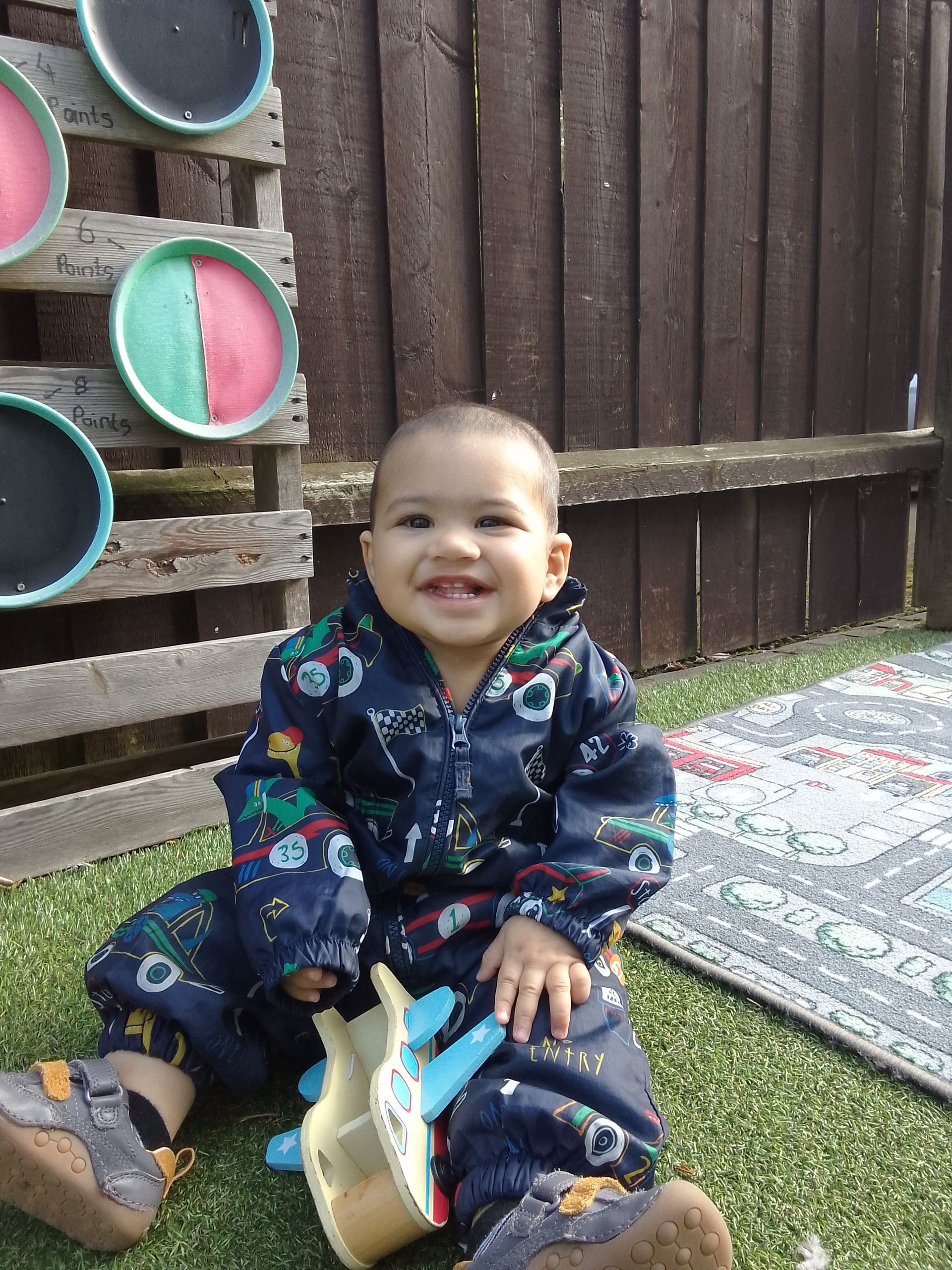 A baby is sitting on the grass holding a toy airplane. Gingerbread