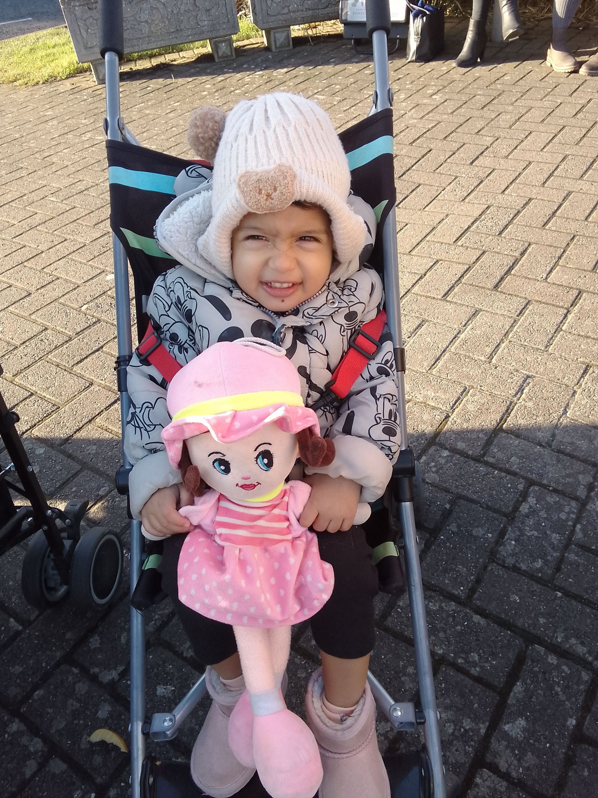 A little girl is sitting in a stroller holding a pink doll Gingerbread