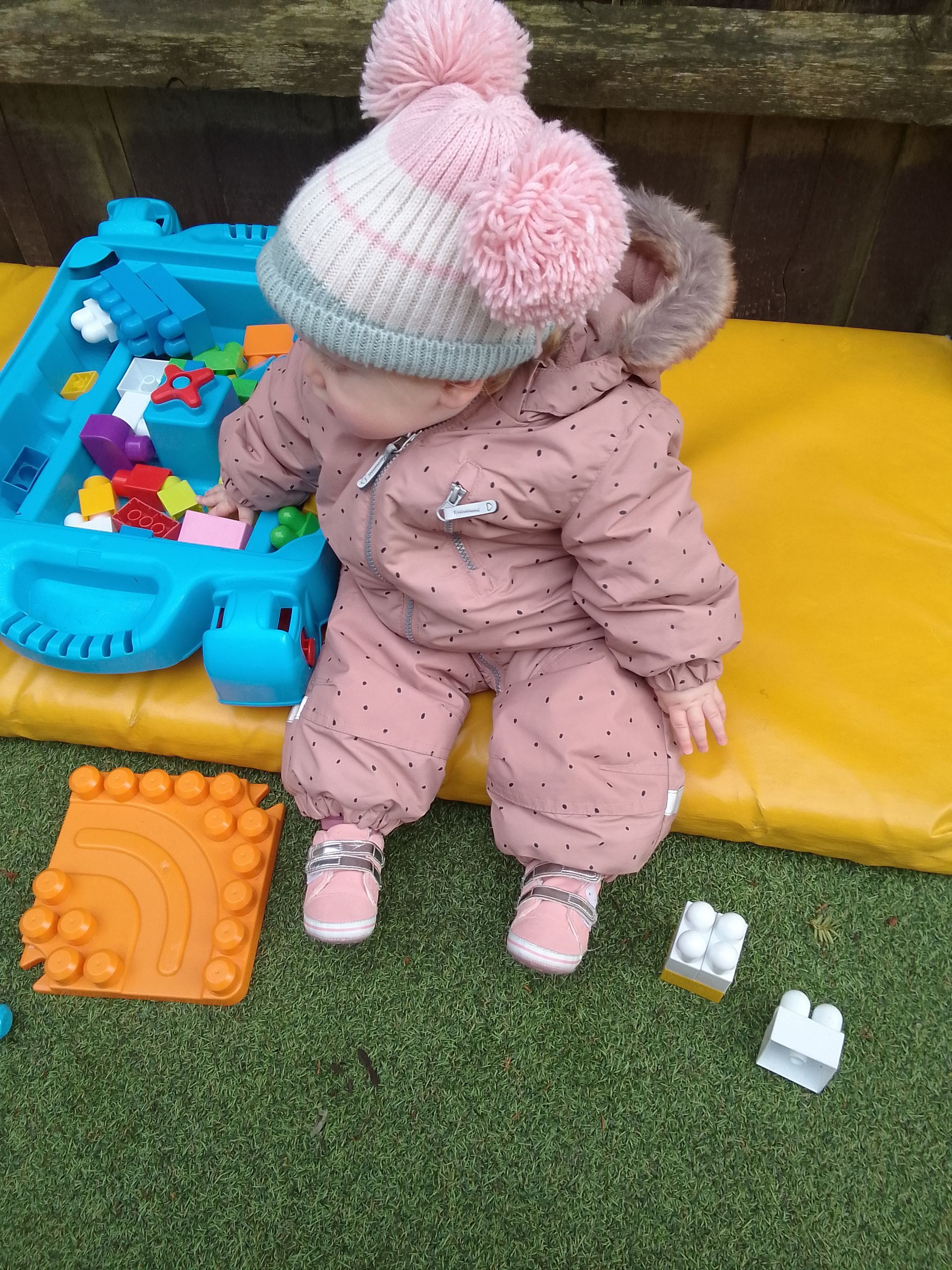 A baby is sitting on a yellow mat playing with toys. Gingerbread