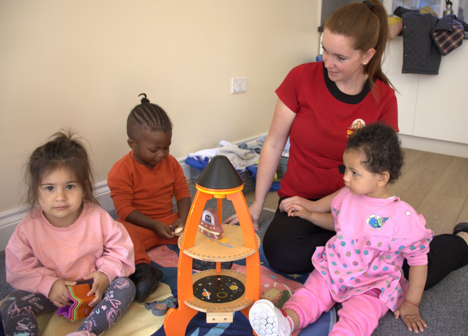 A woman is sitting on the floor with three children playing with a toy rocket. Gingerbread