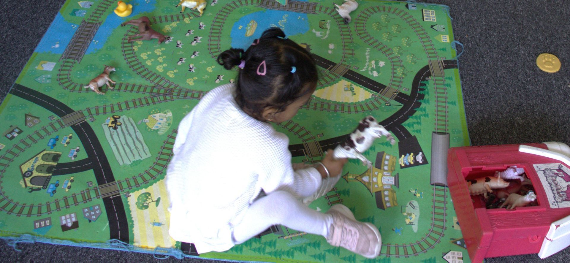 A little girl is playing with a toy train on a rug. Gingerbread