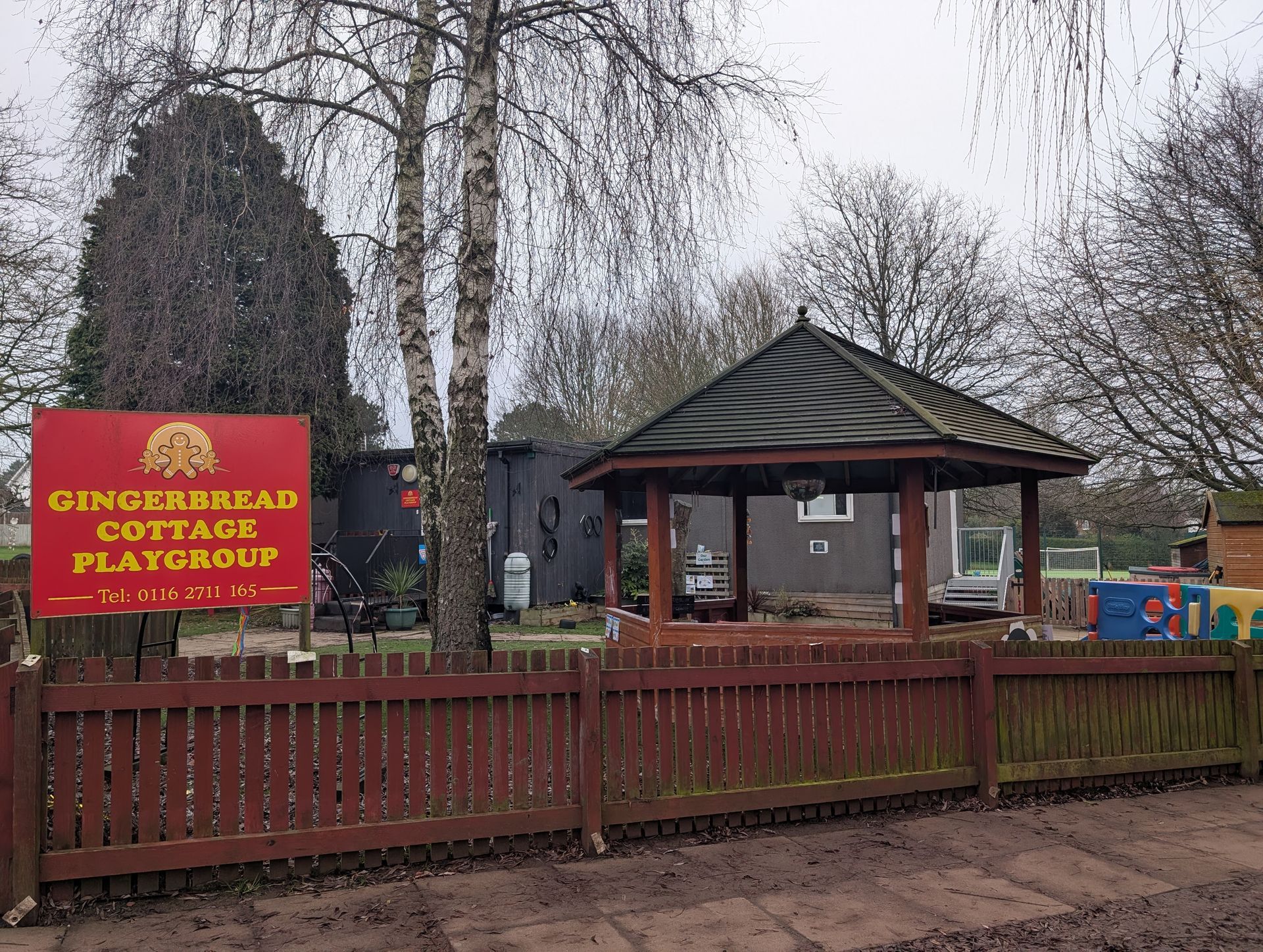A black building with a white door and a wooden fence in front of it. Gingerbread