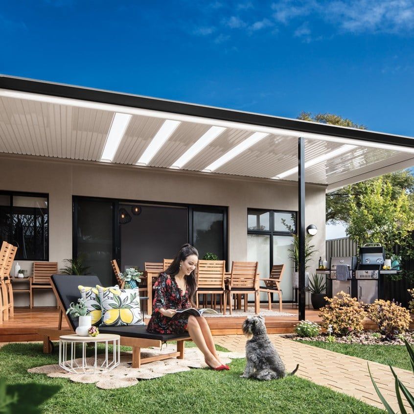 A woman is sitting on a patio with a dog and reading a book.