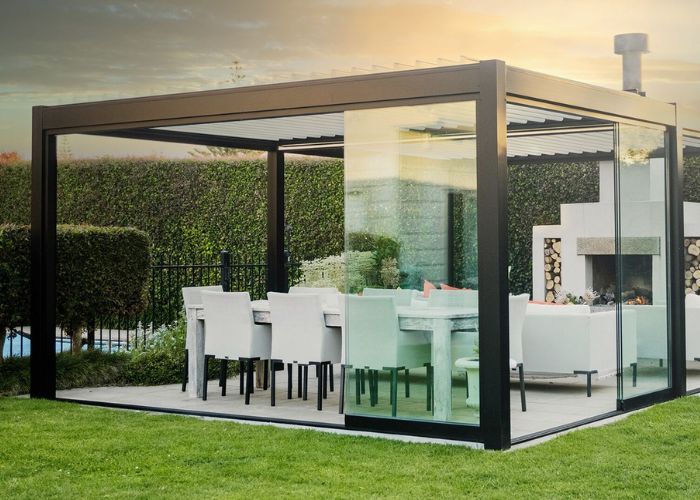 A pergola with a dining table and chairs in a backyard.