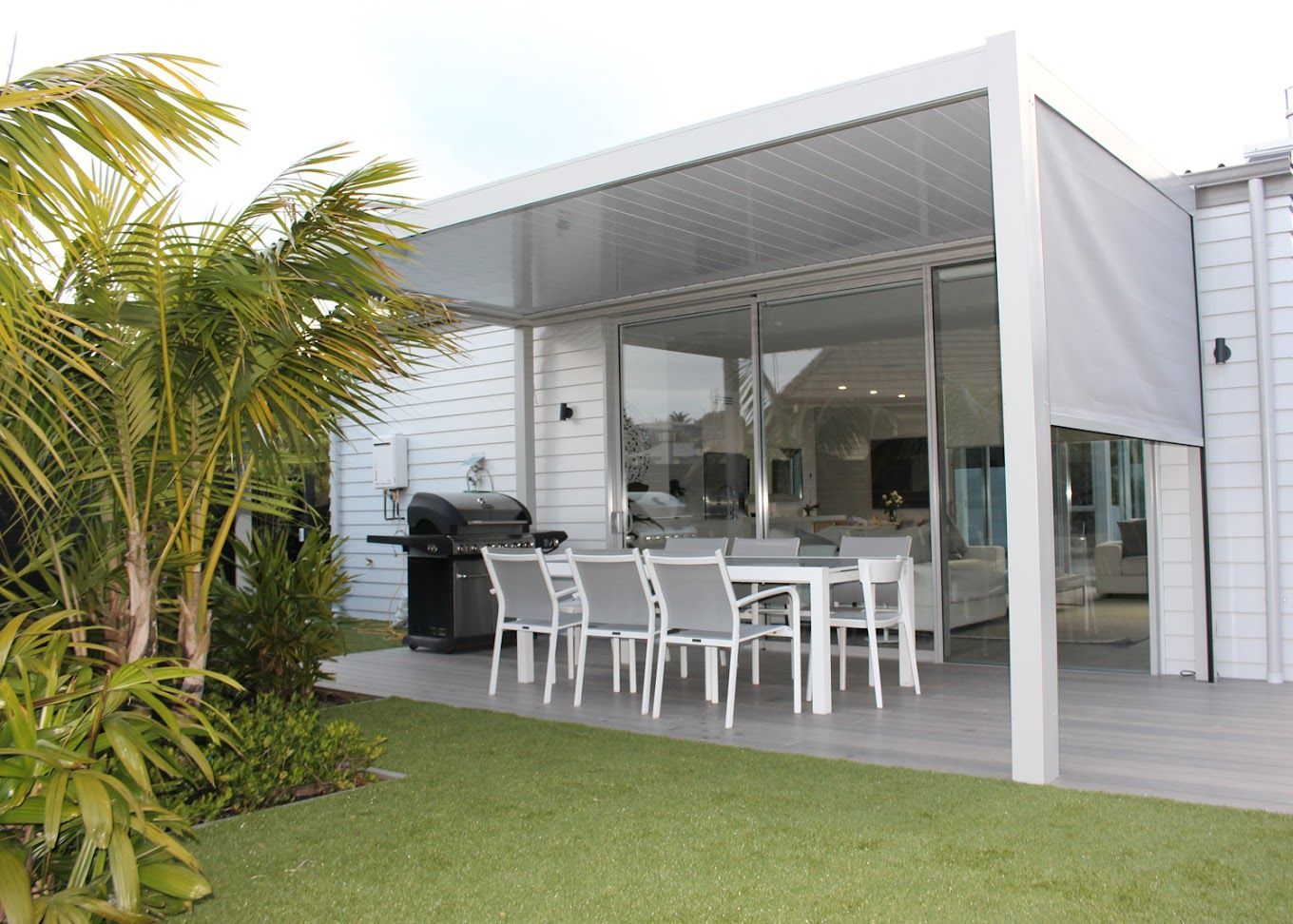 There is a table and chairs under a pergola in the backyard of a house.