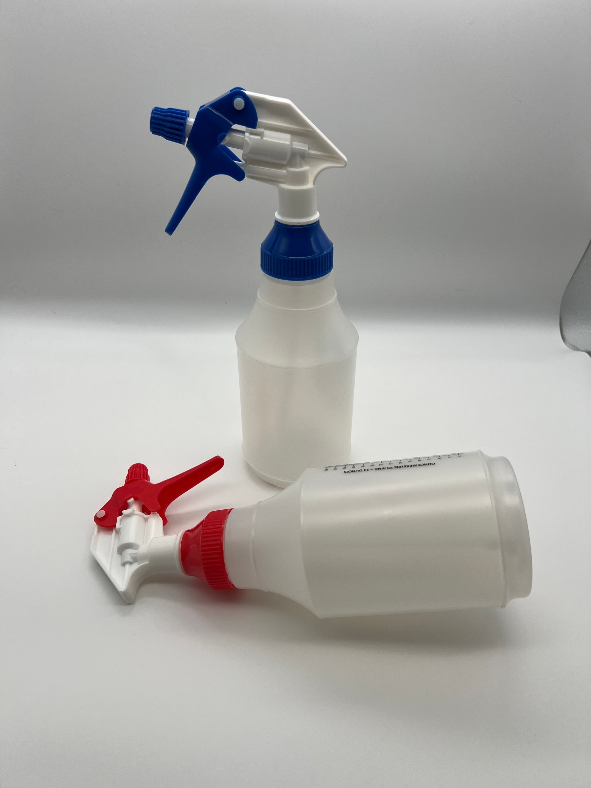 Two spray bottles with red and blue handles are sitting on a white surface.