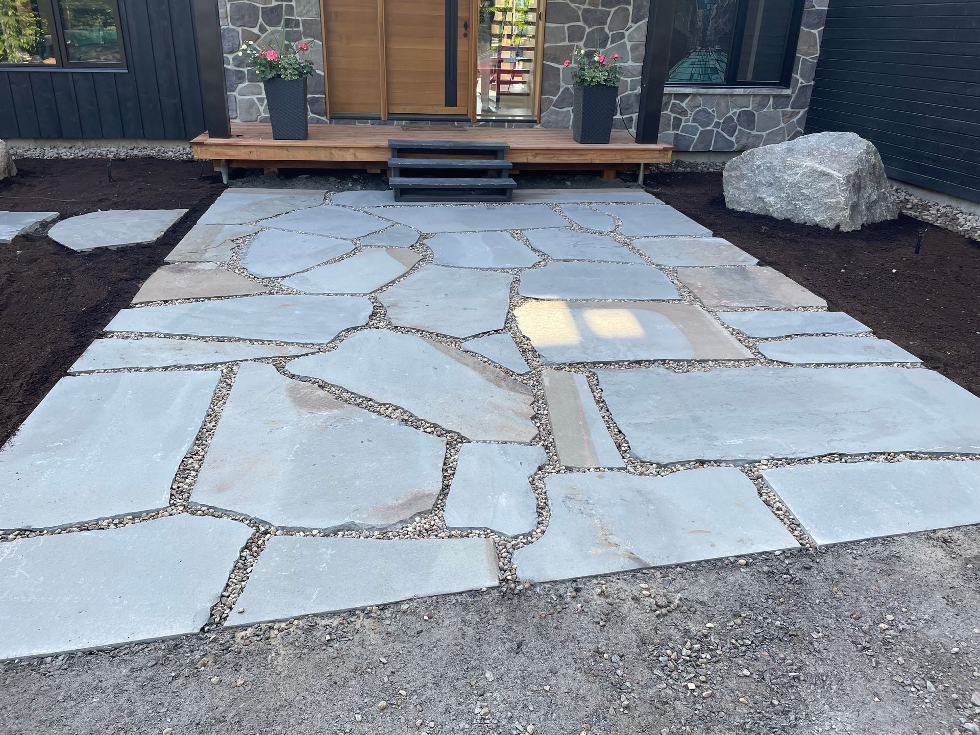 Allée en pierre menant à la porte d'entrée d'une maison moderne. De grosses pierres irrégulières bleu-gris sont séparées par du gravier.