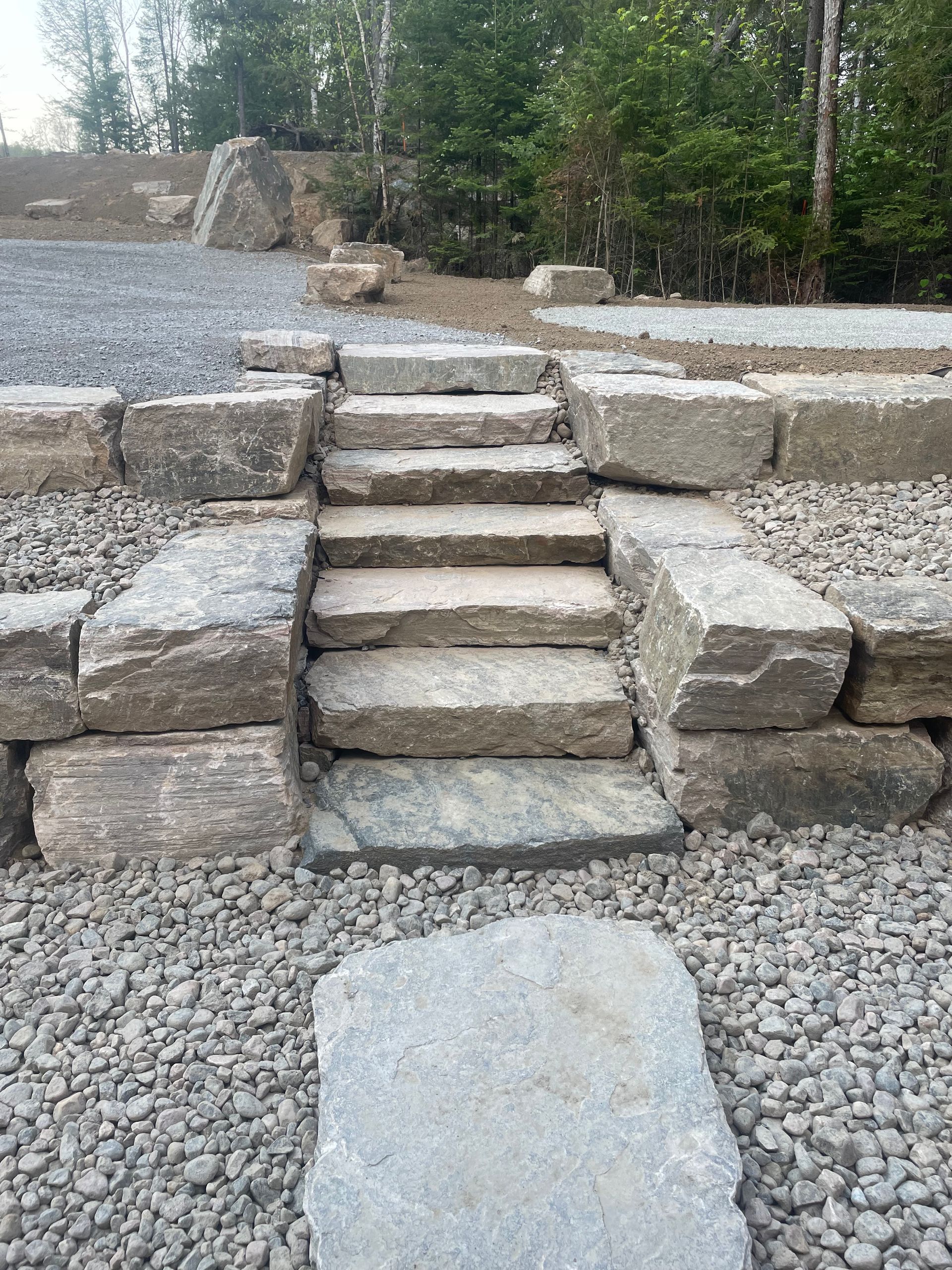 Marches en pierre et murs de soutènement construits sur un chemin de gravier, menant vers le haut en direction des arbres.