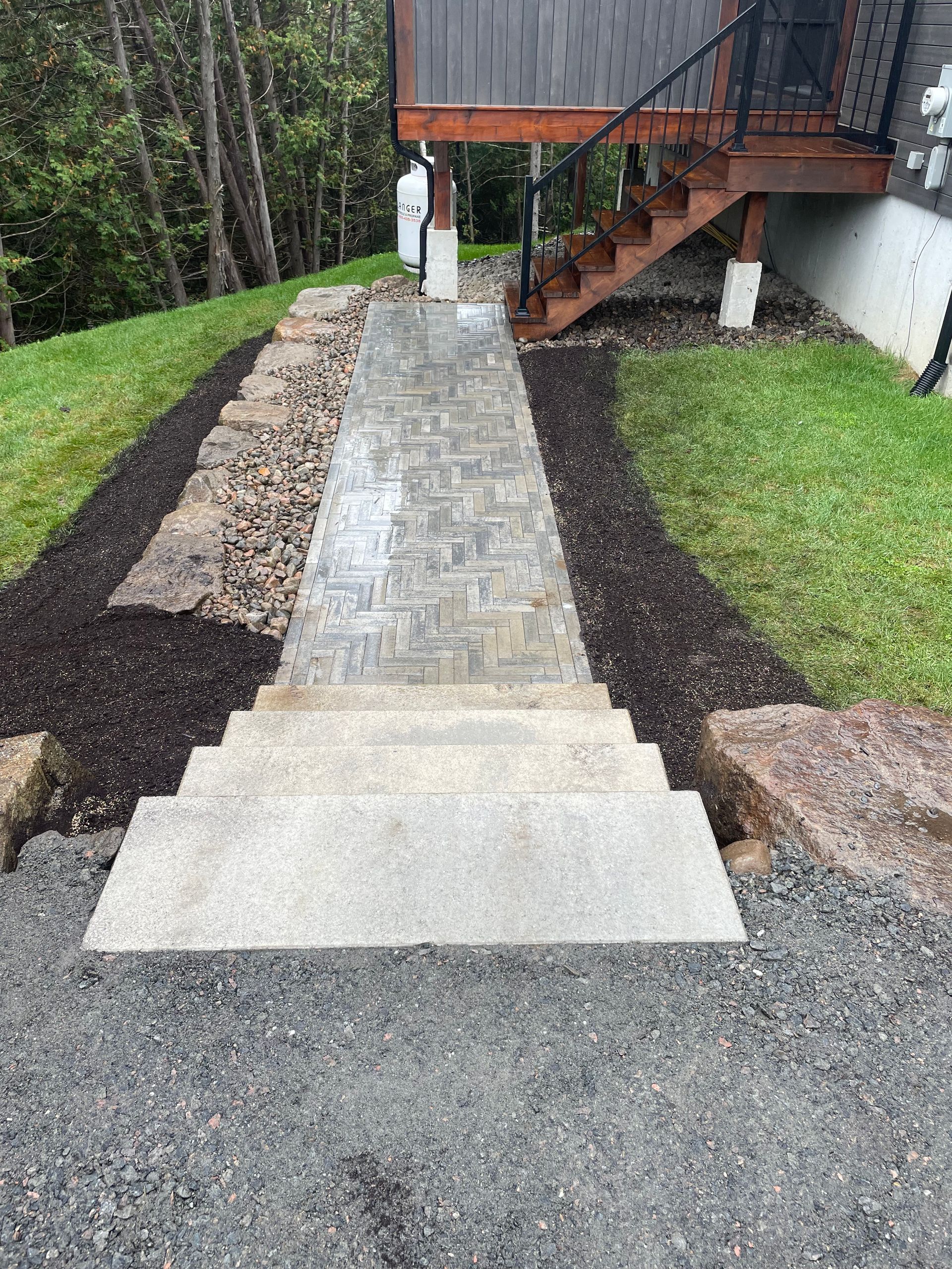 Un chemin pavé avec des marches menant à une terrasse, bordée de paillis et d'herbe.