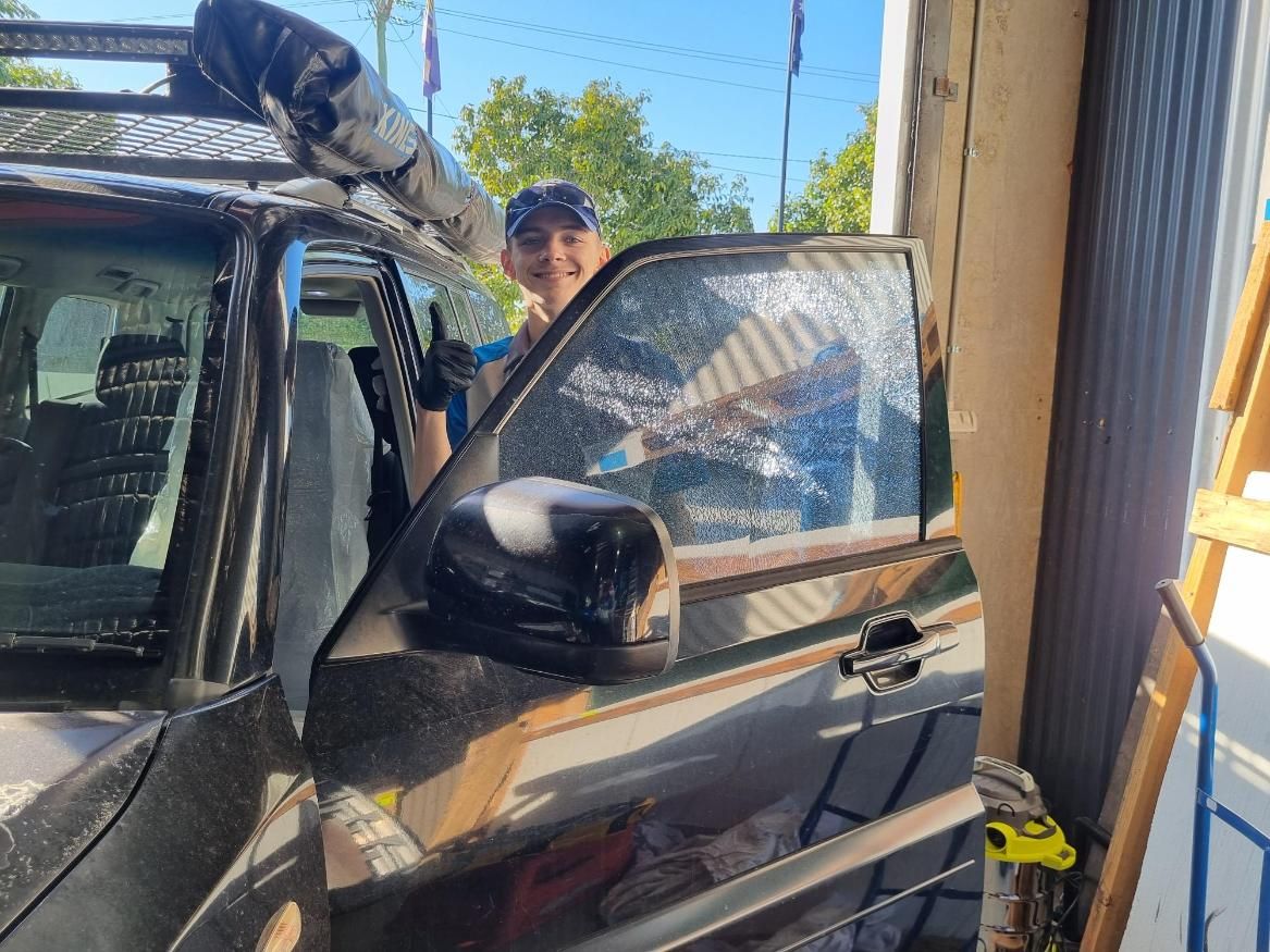 A Man Is Standing Next To A Car With A Surfboard On Top Of It — Australian Specialised Machinery Glass In Mount Louisa, QLD