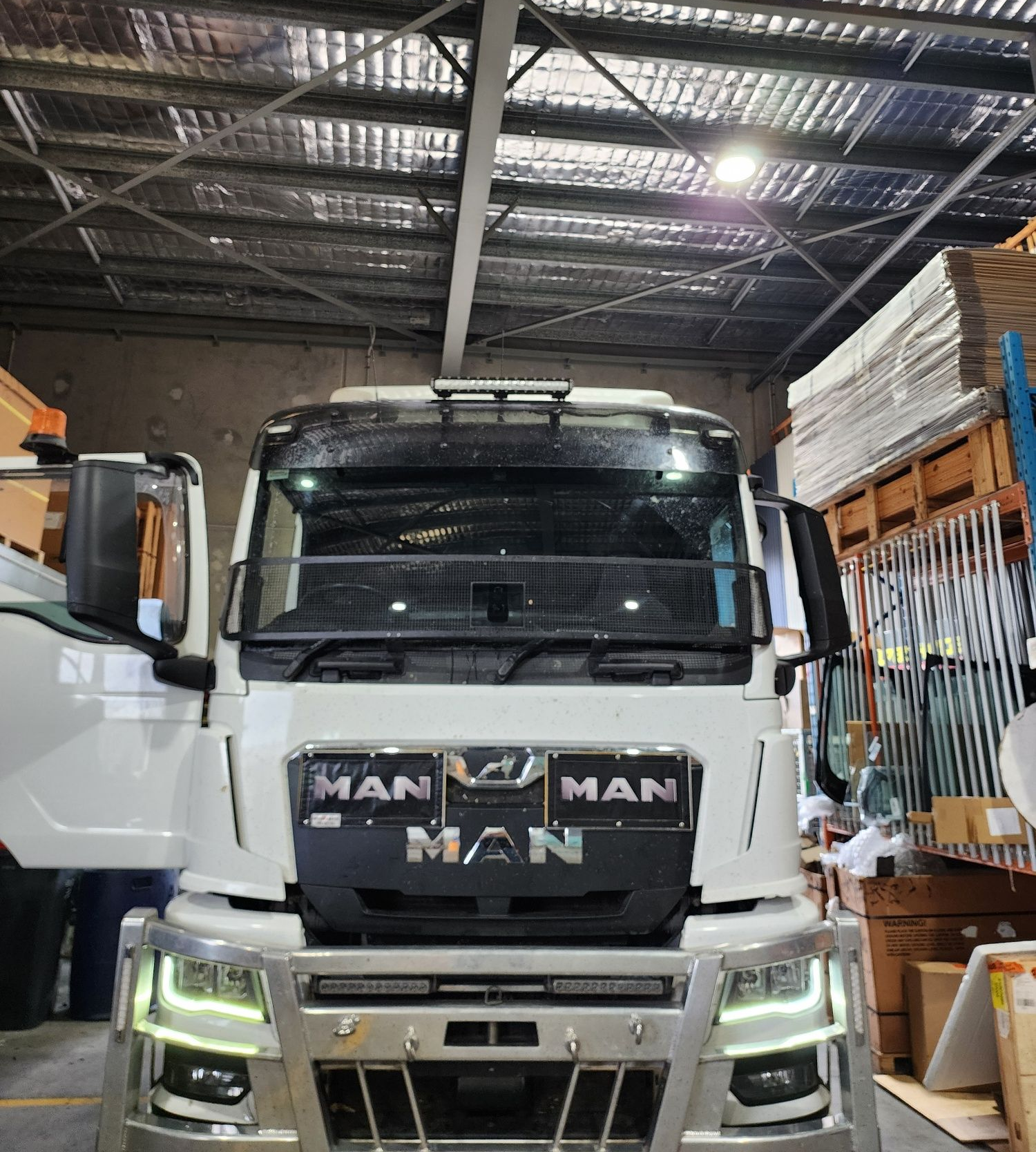 White MAN truck in a warehouse, with open doors and a heavy-duty front bumper — Australian Specialised Machinery Glass In Mount Louisa, QLD
