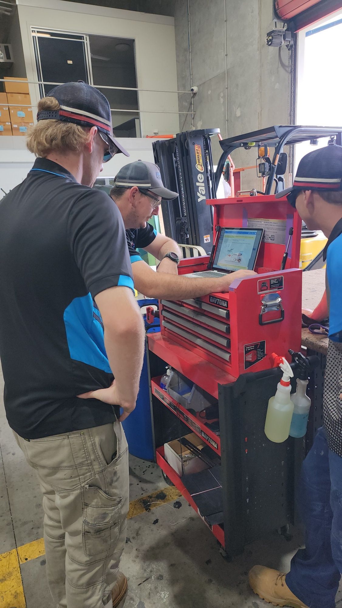 Three mechanics in a warehouse look at a tablet for camera and radar calibration — Australian Specialised Machinery Glass In Mount Louisa, QLD