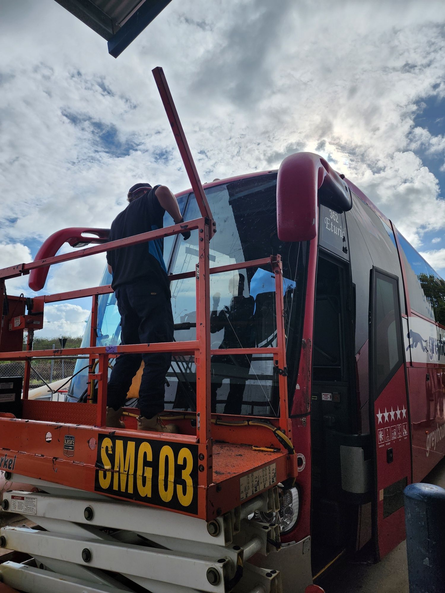 Two people on a lift replacing a bus windshield. The bus is red with blue and white sky. — Australian Specialised Machinery Glass In Mount Louisa, QLD