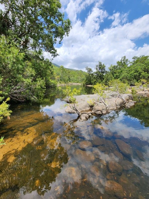 A Calm River Reflecting The Sky, Surrounded By Trees And Rocks — Australian Specialised Machinery Glass In Townsville, QLD