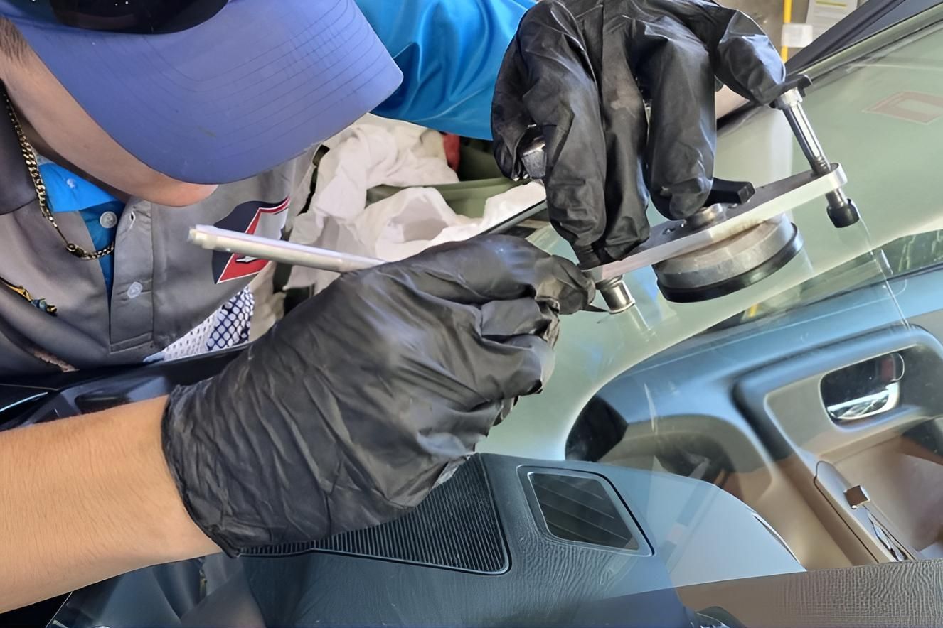 A Man Wearing a Blue Hat and Black Gloves is Working on a Car Windshield — Australian Specialised Machinery Glass In Mount Louisa, QLD