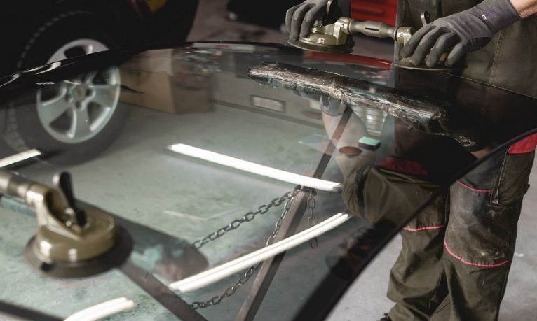 A Man is Fixing a Windshield on a Car in A Garage — Australian Specialised Machinery Glass In Mount Louisa, QLD