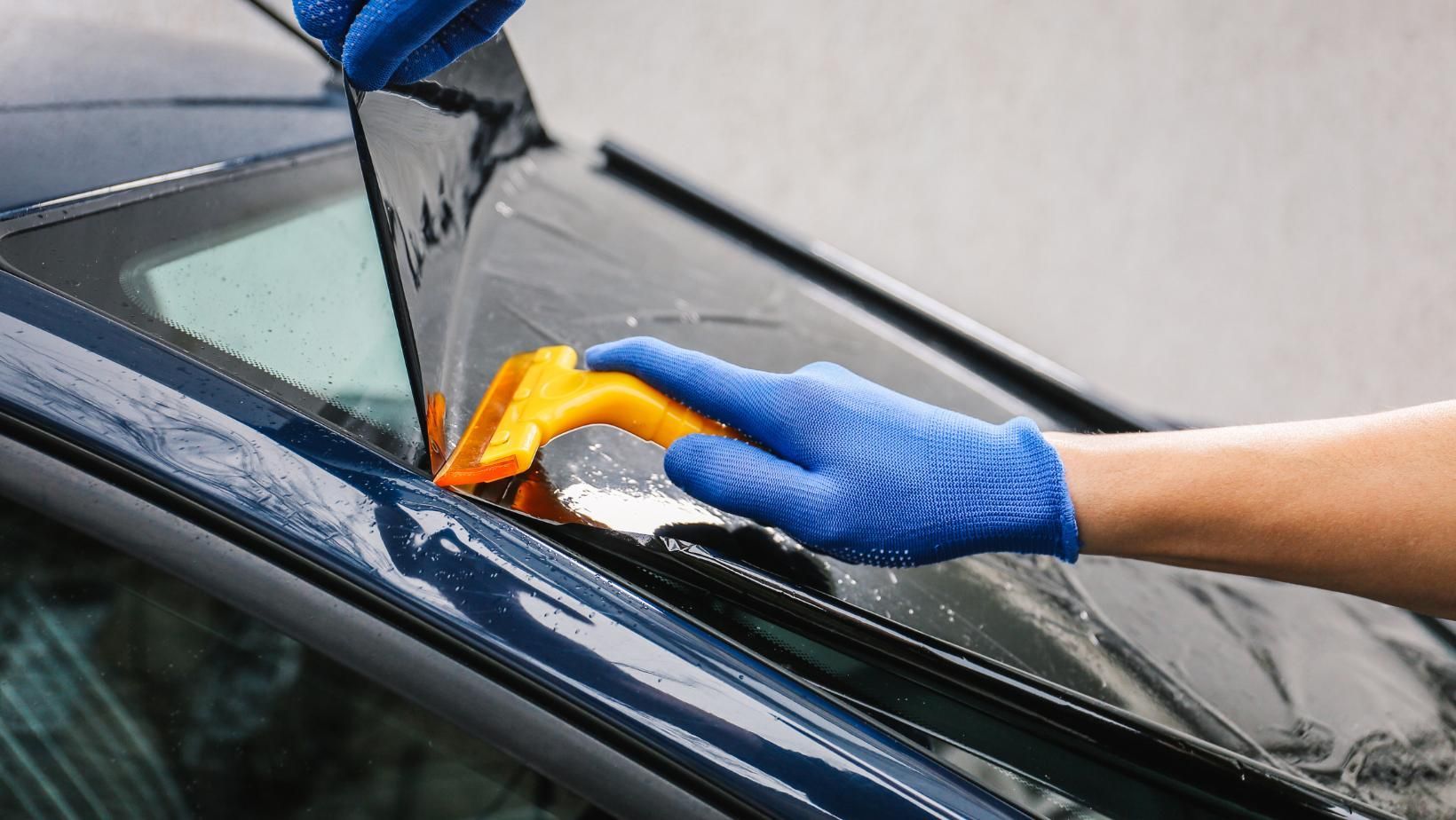 Person Applying Window Tint to a Car, Using a Squeegee and Wearing Blue Gloves — Australian Specialised Machinery Glass In Emerald, QLD