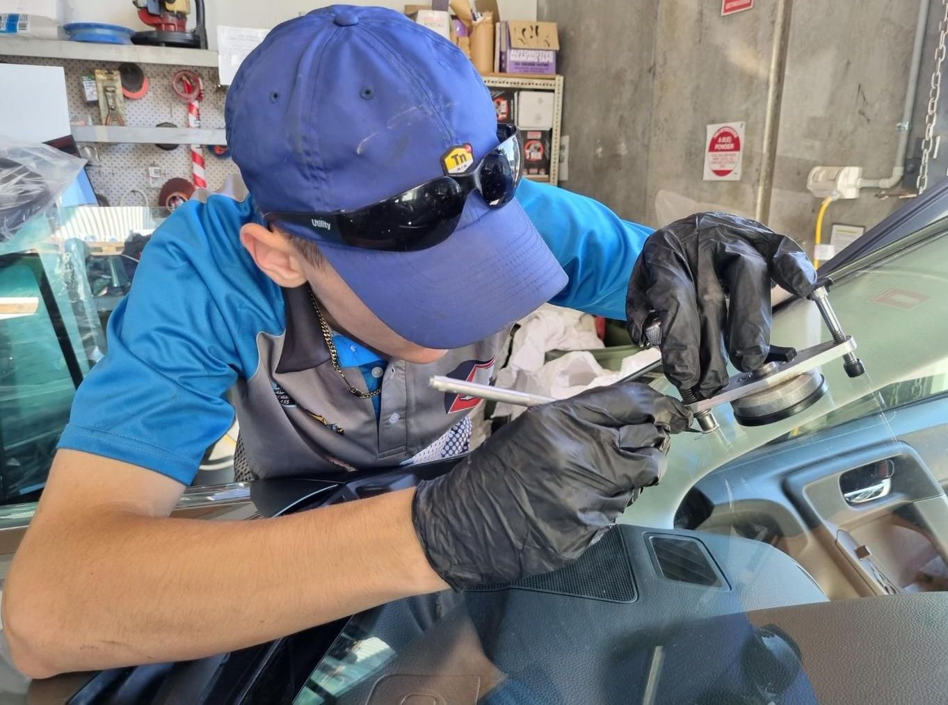 A Man Wearing a Blue Hat and Black Gloves is Working on a Car Windshield — Australian Specialised Machinery Glass In Mount Louisa, QLD