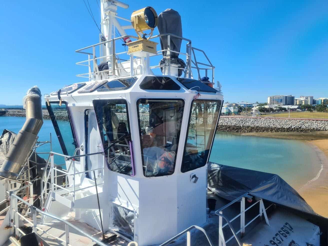 A Man Is Sitting In The Cockpit Of A Boat In The Water — Australian Specialised Machinery Glass In Mount Louisa, QLD