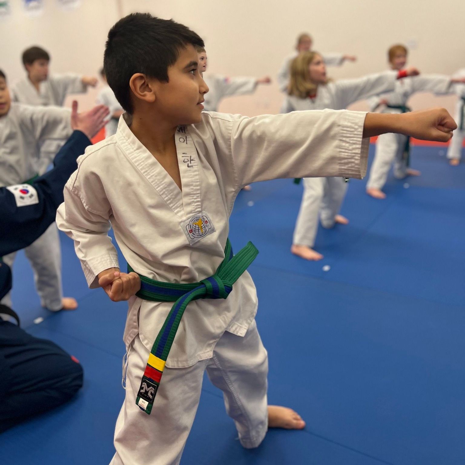 A man is kneeling down next to a young boy in a taekwondo class.