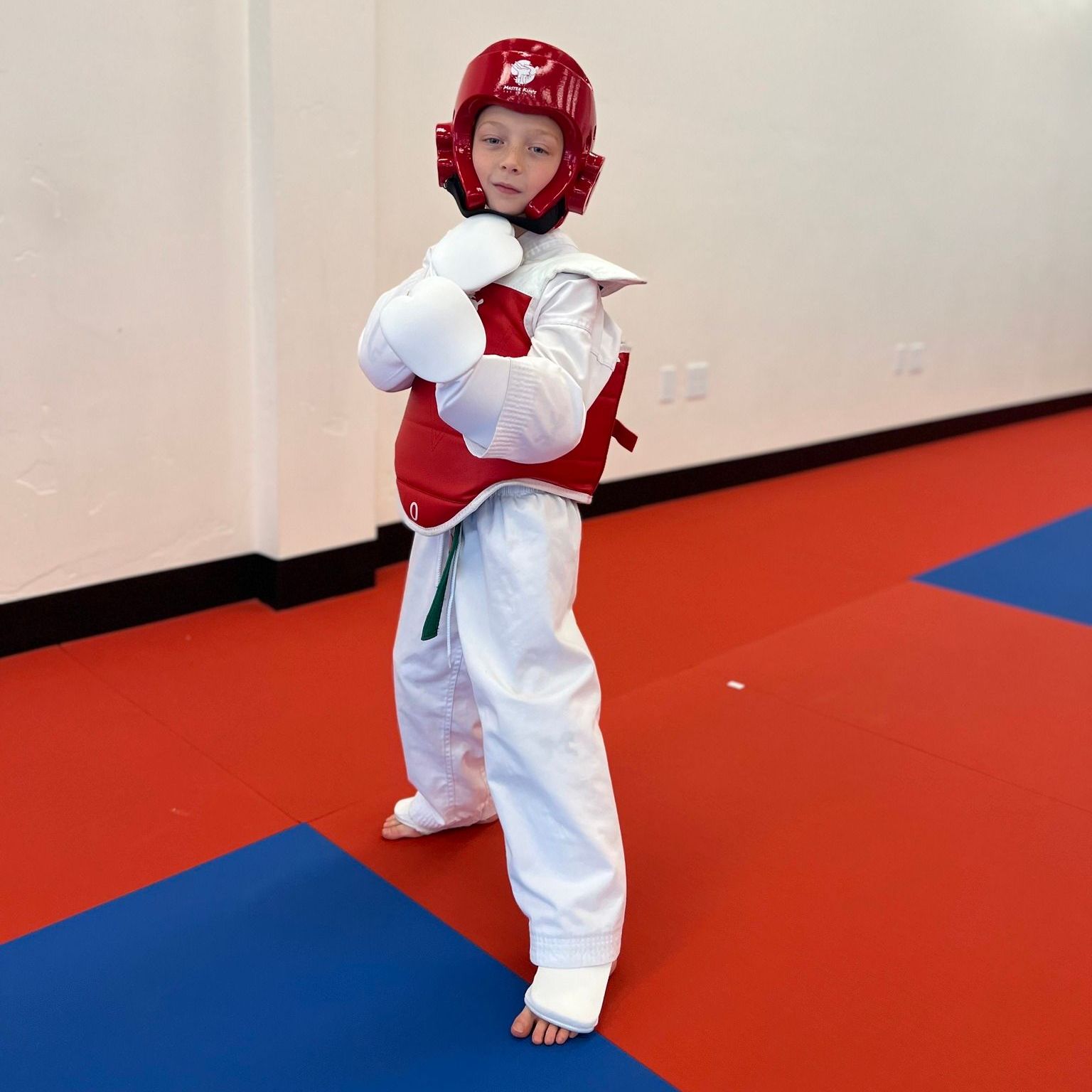 A young girl in a karate uniform is sitting on the floor.