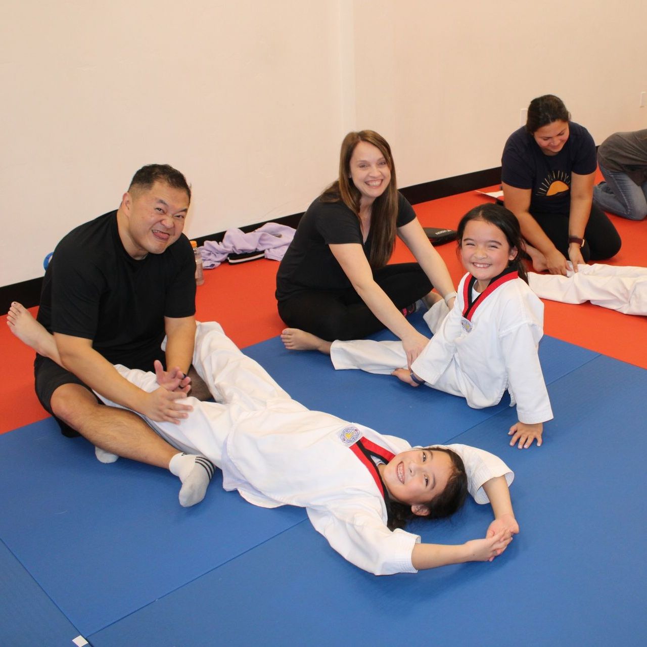 A young girl in a karate uniform is sitting on the floor.