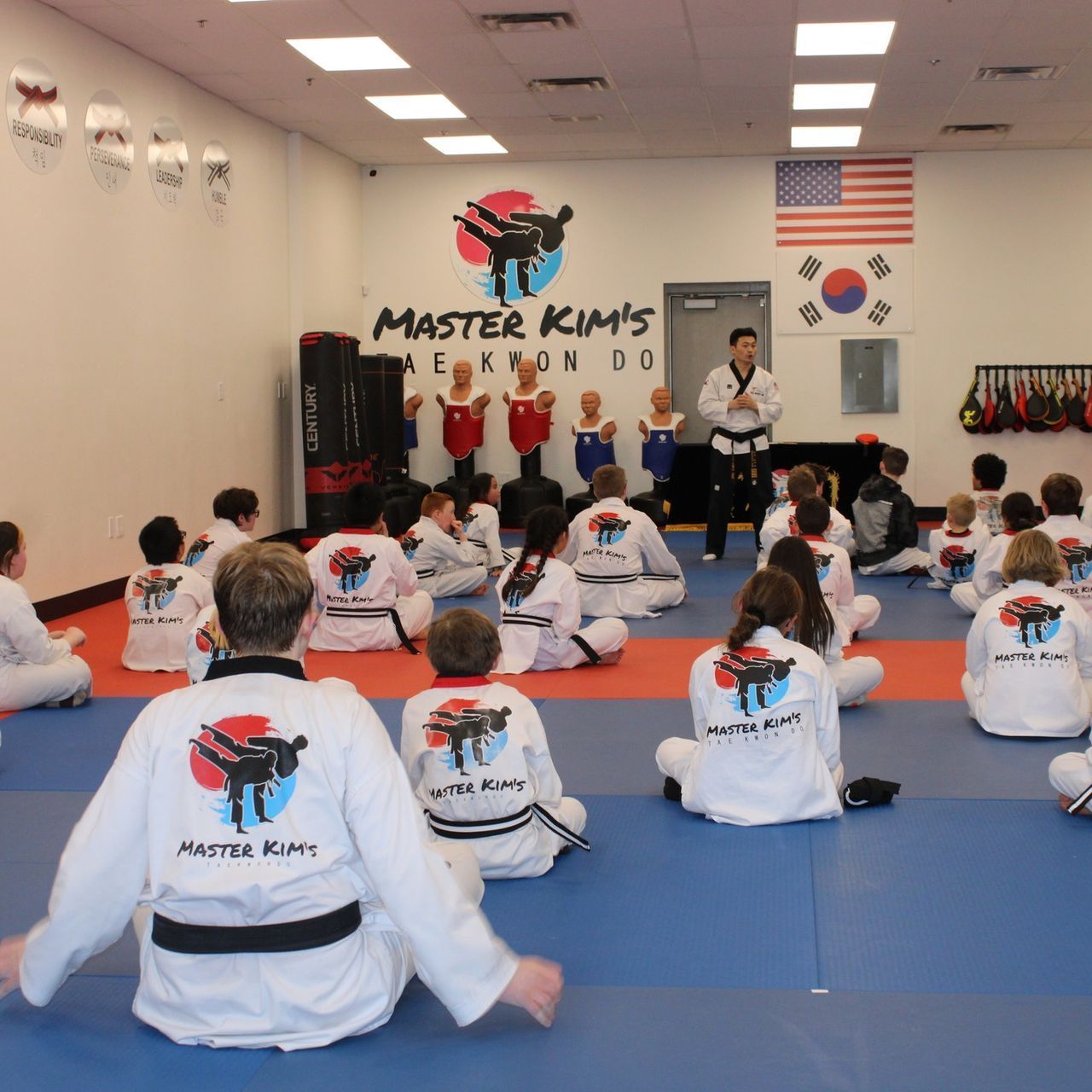 A group of children are practicing karate with a teacher in a gym.