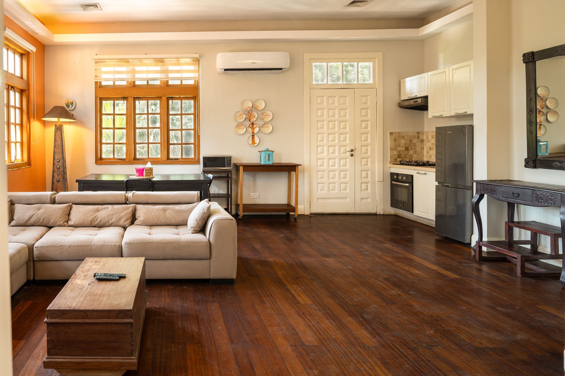 Modern living room with a large beige sectional, wood coffee table, dark hardwood floors, and an adjacent kitchen area.