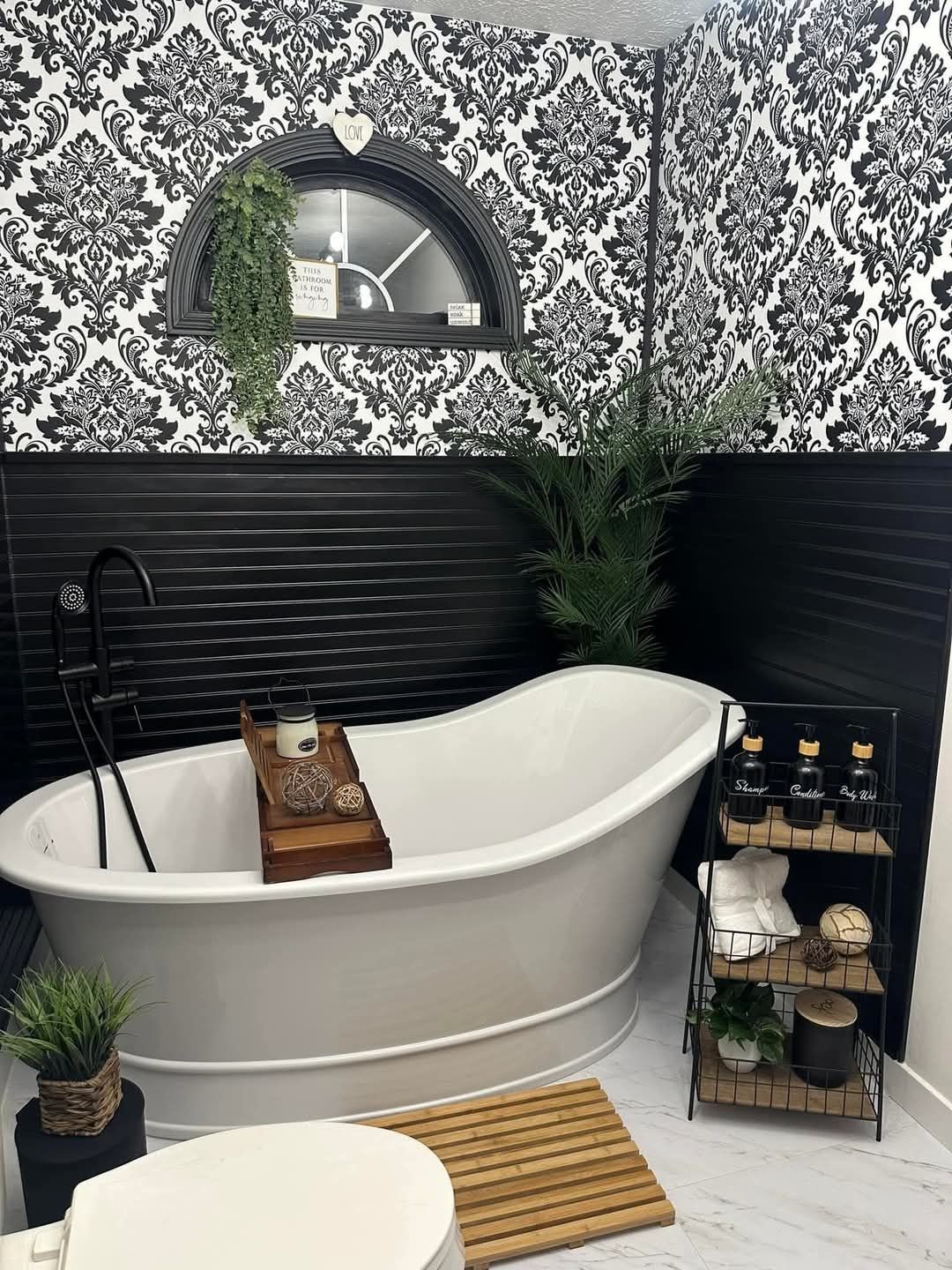 A bathroom with a bathtub , toilet , and black and white wallpaper.