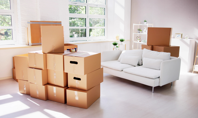 Boxes stacked in a room with a white couch, indicating a move; bright sunlight.