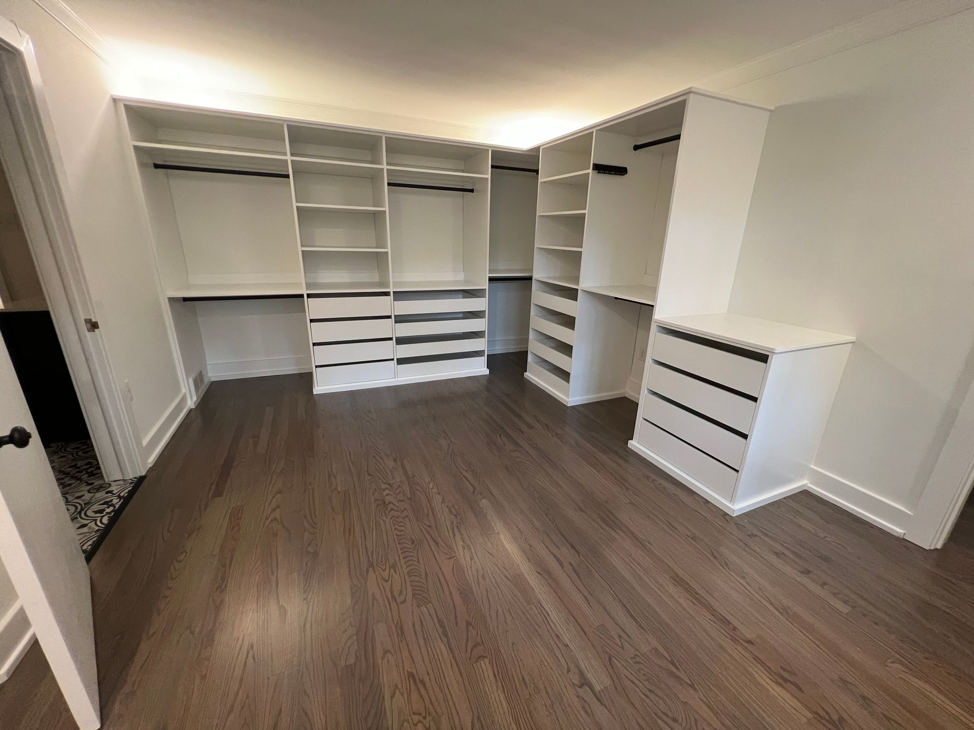 Walk-in closet with white shelving, drawer units, and hanging rods against walls over dark wood flooring.
