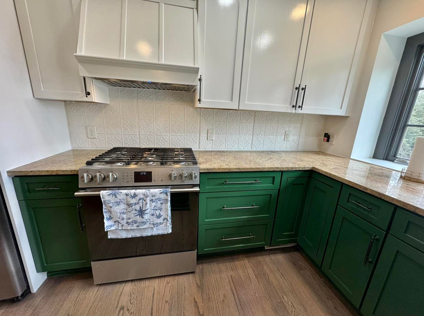 A kitchen corner featuring a stainless steel stove with a white hood, speckled countertops, and green cabinets.